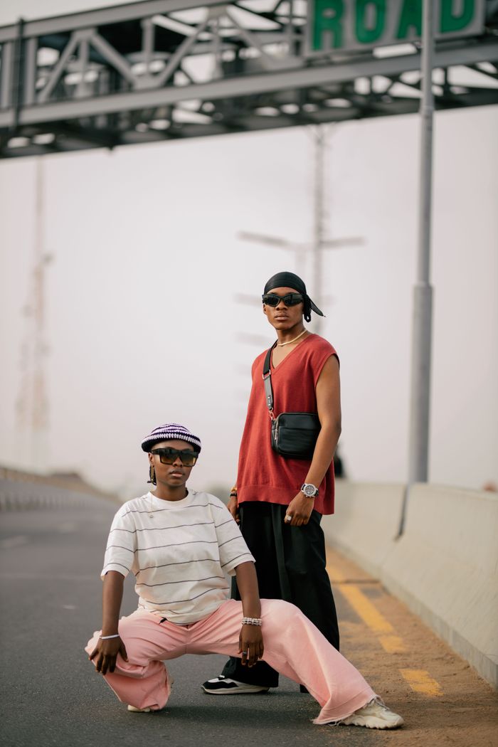 Trendy adults in stylish outfits pose confidently on a city street under a road sign.