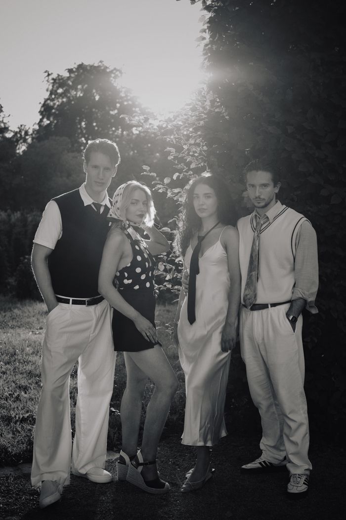 gallery-2 Black and white photo of four adults in vintage attire posing outdoors at sunset.