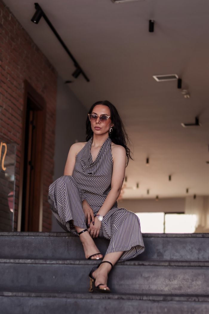 gallery-5 Fashionable woman in striped outfit and sunglasses posing confidently indoors.