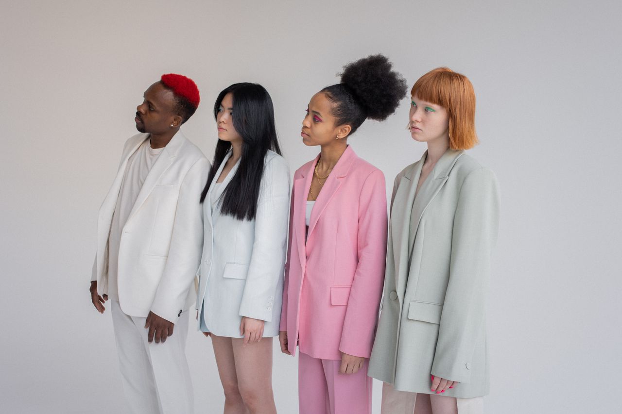 services-01 Multiethnic female models and man wearing elegant outfits standing in line against gray background and looking away with attention